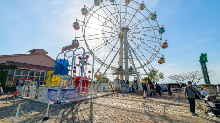 晴れた日の遊園地にある大きな観覧車とアトラクションの風景