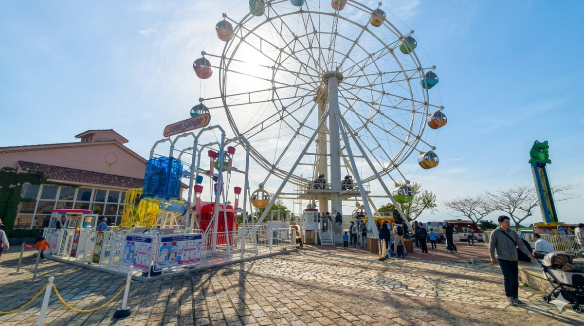 晴れた日の遊園地にある大きな観覧車とアトラクションの風景